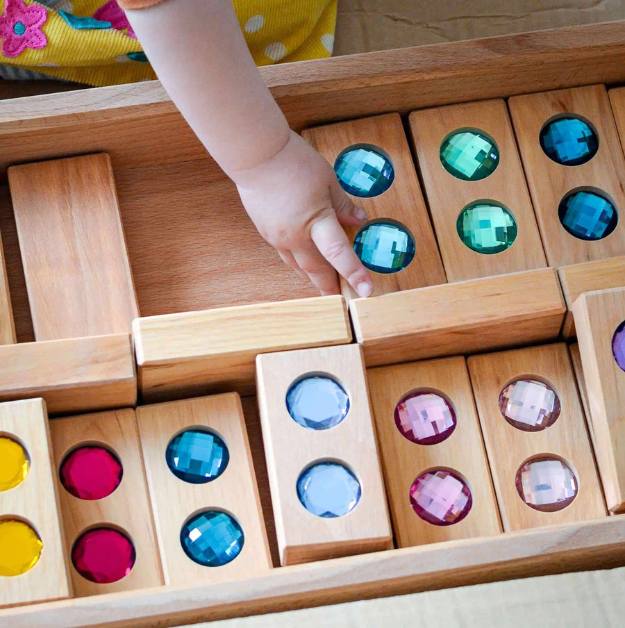 Child's hand placing a Bauspiel Color Track gem block back in the wooden tray