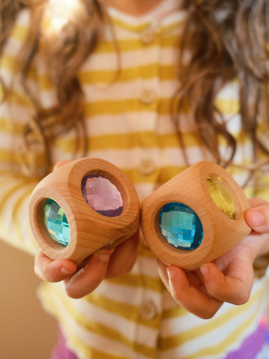 A child holding two Bauspiel Magic Cube Pastel wooden cubes with pastel gems